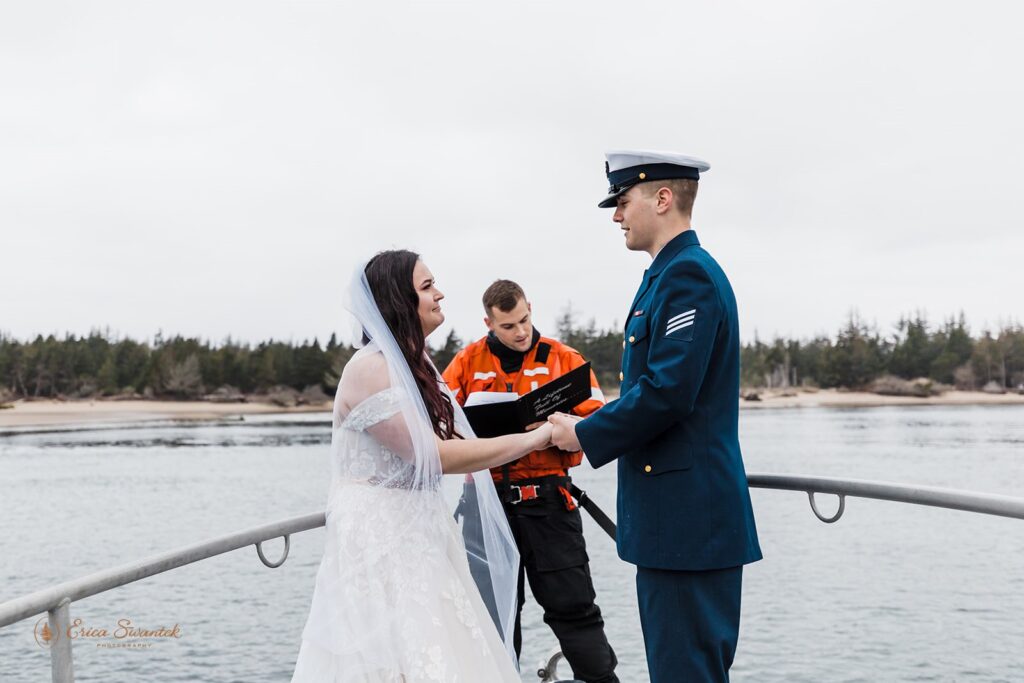 A coast guard couple holds hands while eloping on a boat with an officiant off the Oregon Coast.