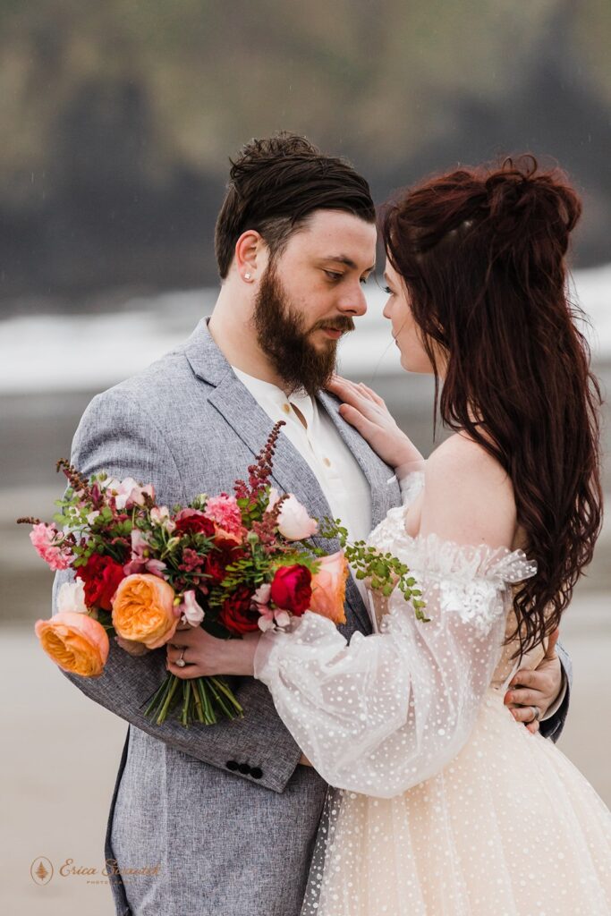 A groom holds his bride close while she carries a bouquet of colorful wedding florals. 