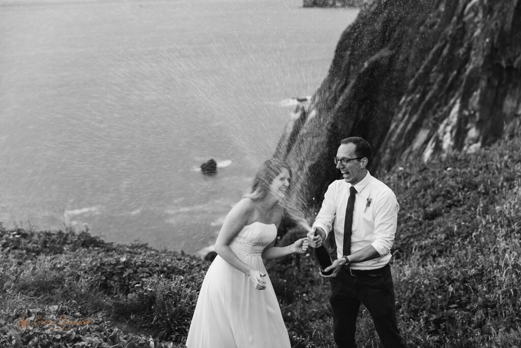 A couple pops champagne together in celebration of their Oregon Coast elopement. 