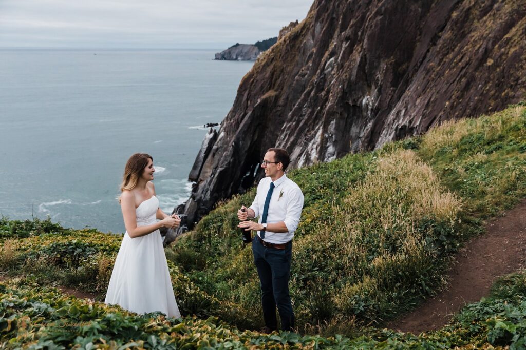 A groom prepares to pop celebratory champagne along an Oregon Coast lookout.