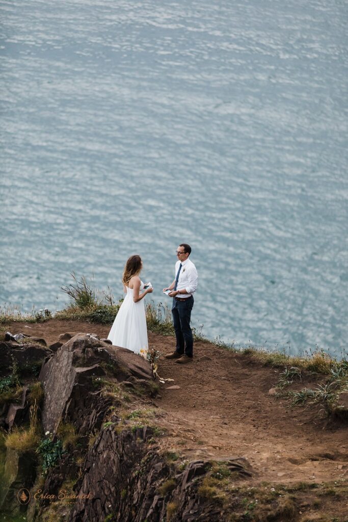 A Oregon Coast elopement couple stands on an a cliff overlook sharing vows with one another.