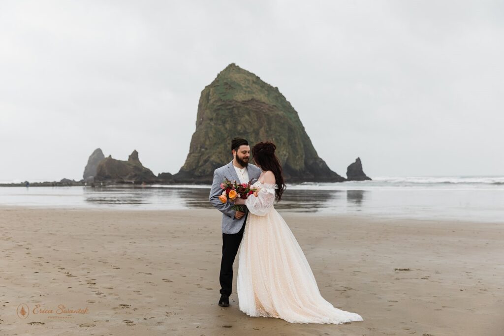 A bride in a champagne-colored wedding dress poses with her partner at Cannon Beach. 