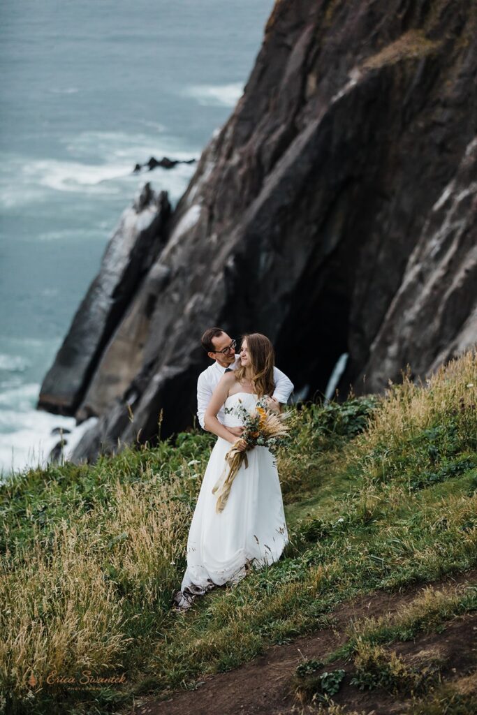 A couple sits in a meadow while taking Oregon Coast wedding portraits along Elk Flats Trail. 