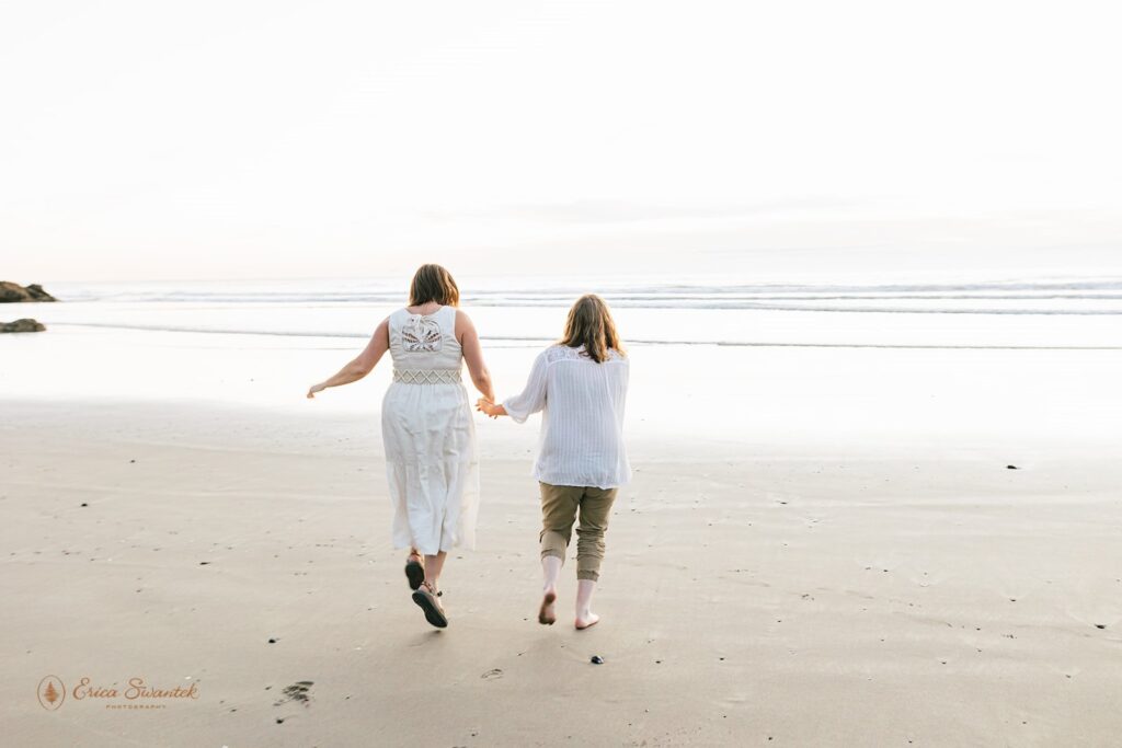 A couple holds hands while walking along Neptune Beach in Oregon during their coastal elopement.