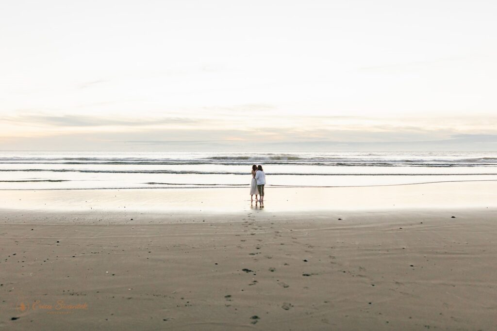 A couple is seen in the distance embracing during Sunset at Neptune Beach, Oregon. 