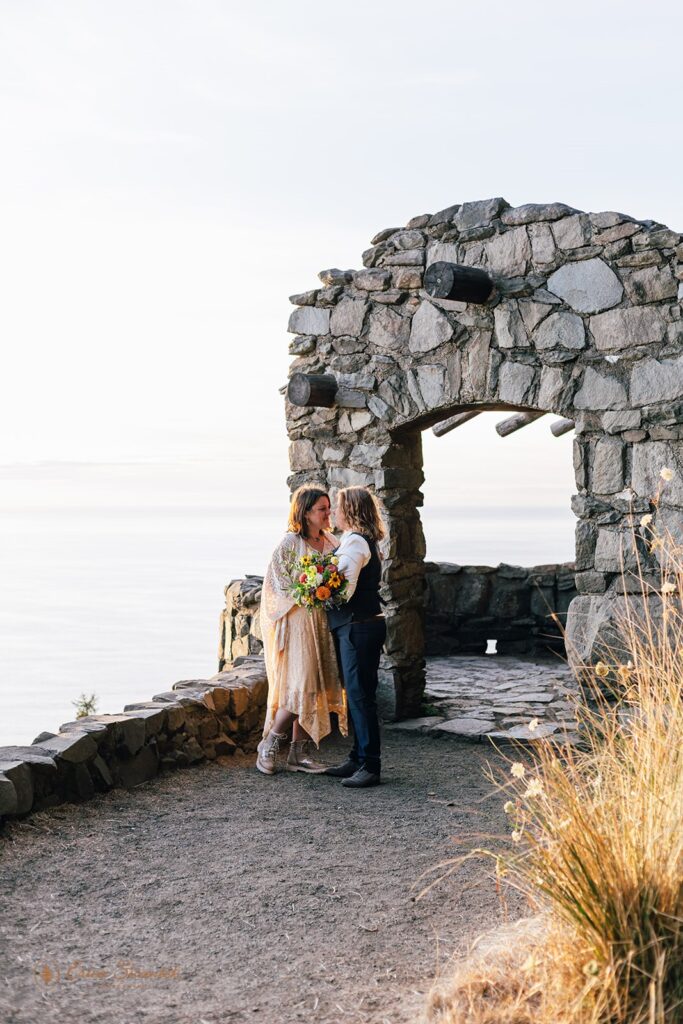 A couple poses for elopement portraits near a pavilion Cape Perpetua Scenic Area.