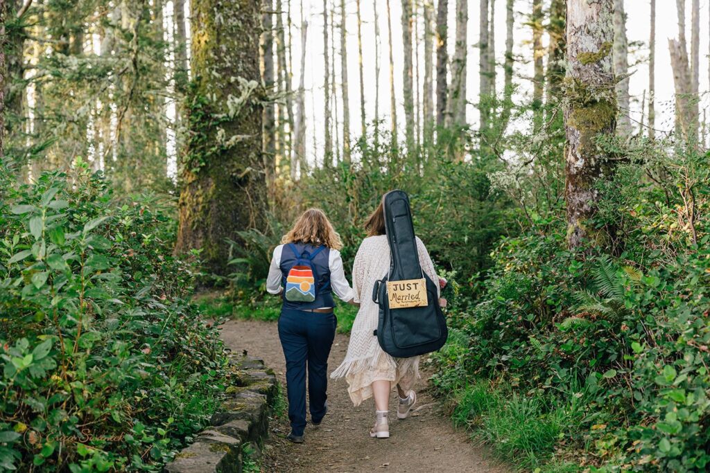 A couple elopes in an Oregon forest while wearing packs, one of which is a guitar case holding a just married sign.