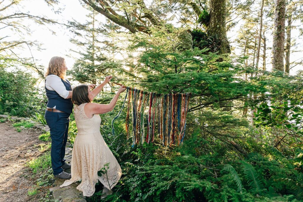 A couple hands a decorative art piece from trees during their forest elopement at Cape Perpetua Scenic Area.