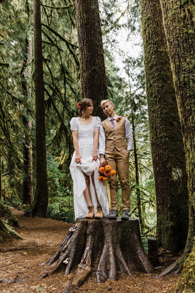 An adventure elopement couple shows off their hiking boots while standing on a tree stump.