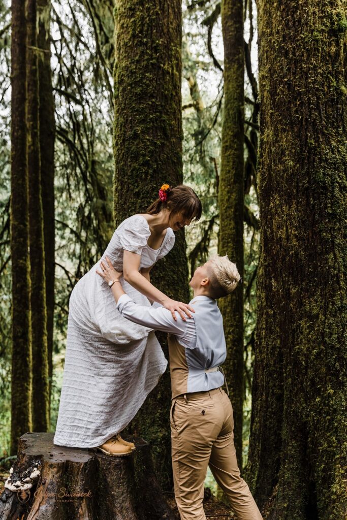 A woman's partner helps her down off a tree stump during their forest wedding in Oregon. 