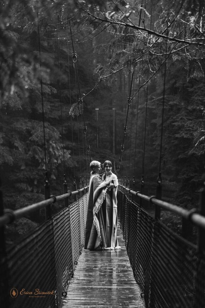A couple cuddles beneath a blanket on a suspension bridge along Drift Creek Falls Trail in Siuslaw National Forest. 