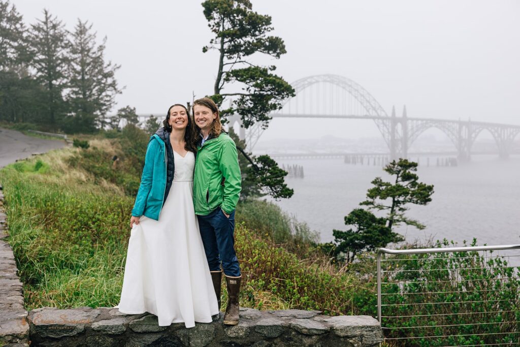 elopement couple posing for their elopement in newport with a bridge covered in fog in the backdrop