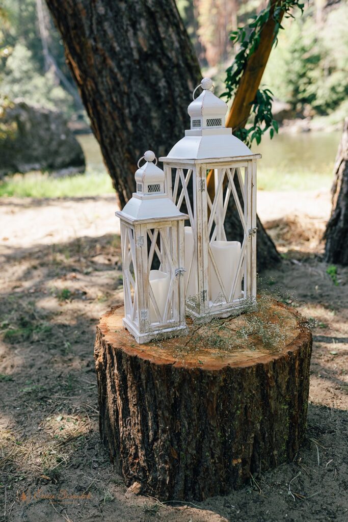 Two white wedding lanterns on a tree stump. 