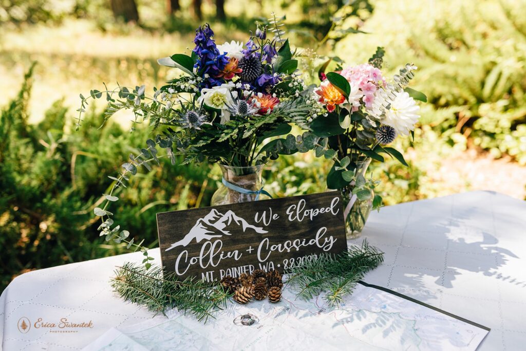 An elopement sign near colorful floral arrangements in vases that are set atop a map of Washington State. 
