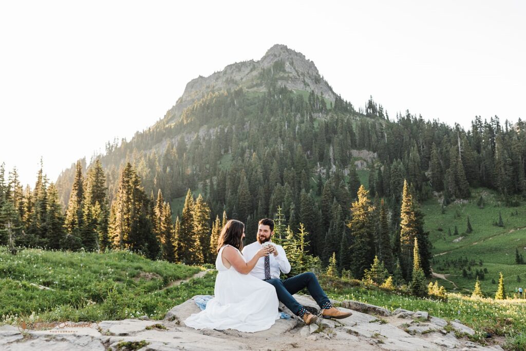A Mt. Rainier elopement couple sits on a rock near Tipsoo Lake at Sunset drinking beers. 