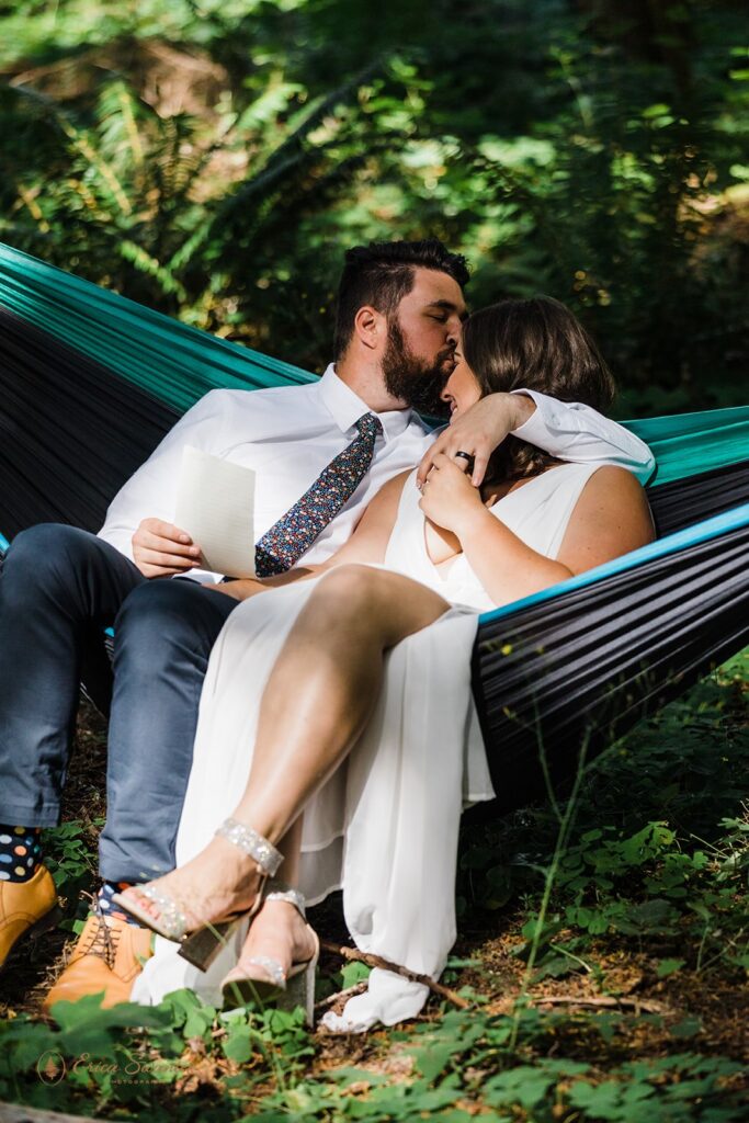A bride and groom sit with one another in a two person hammock while reading private vows before their Mt. Rainier elopement. 