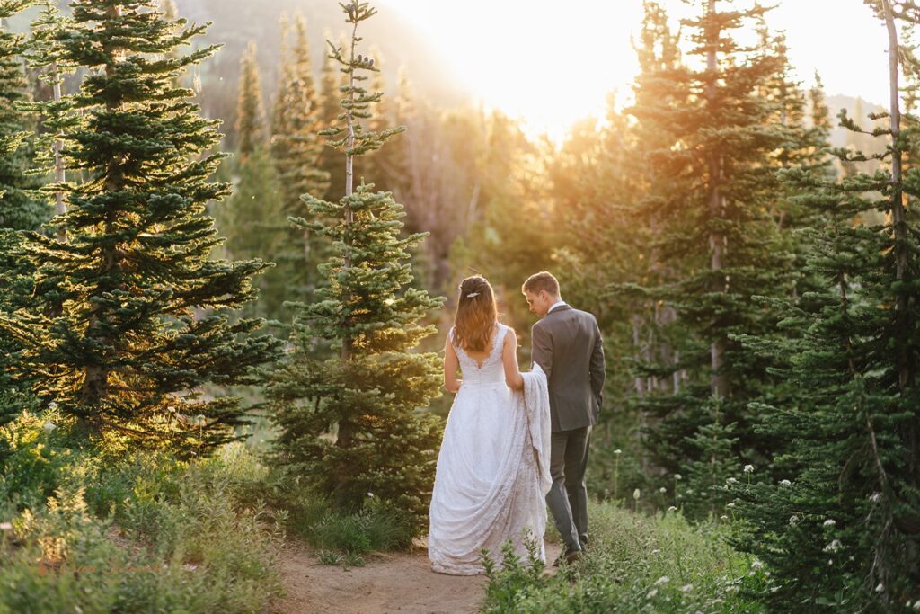 A woman in a long, white wedding gown hikes with her groom, wearing a suit, along a hiking trail in the Sunrise Area of Mt. Rainier National Park. 