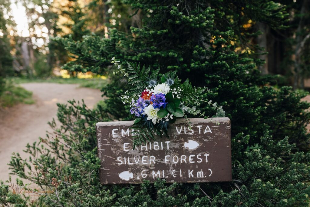 A hiking trail sign with a colorful wedding bouquet draped over the top. 
