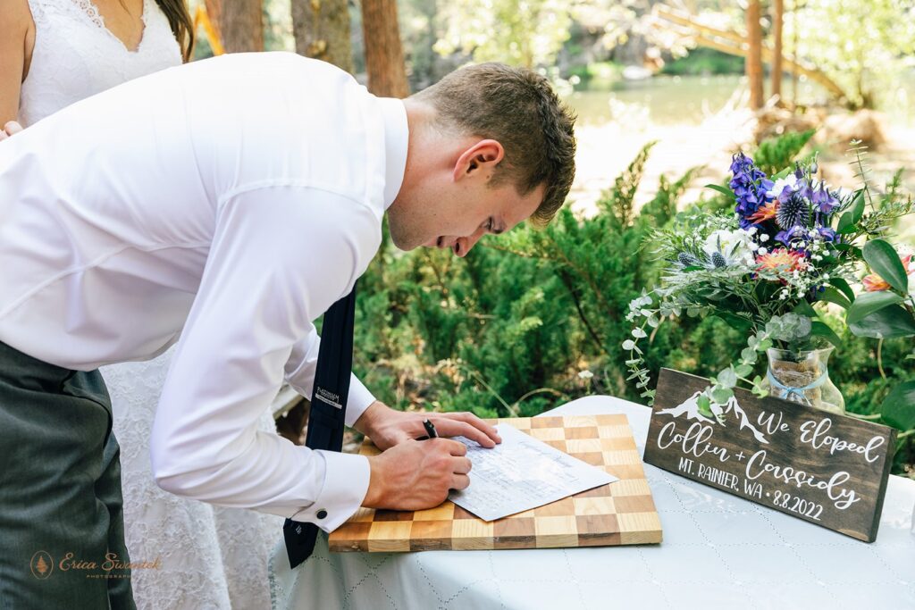 A groom signs a Washington marriage license at an outdoor elopement at Whistlin' Jack's.