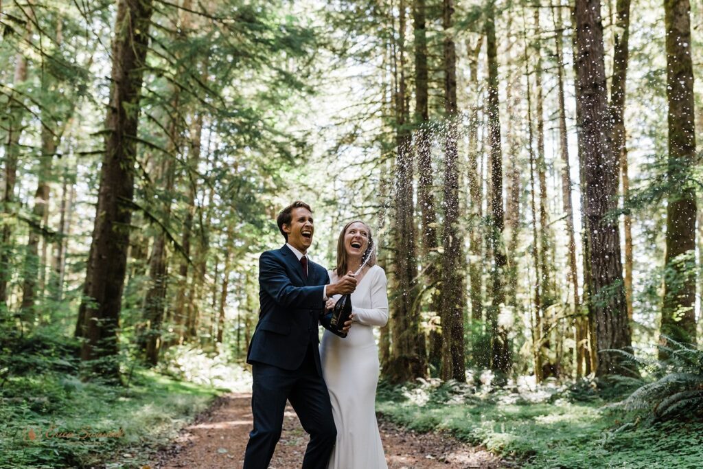An adventure elopement couple pops champagne in an evergreen forest in Mt. Rainier National Park. 