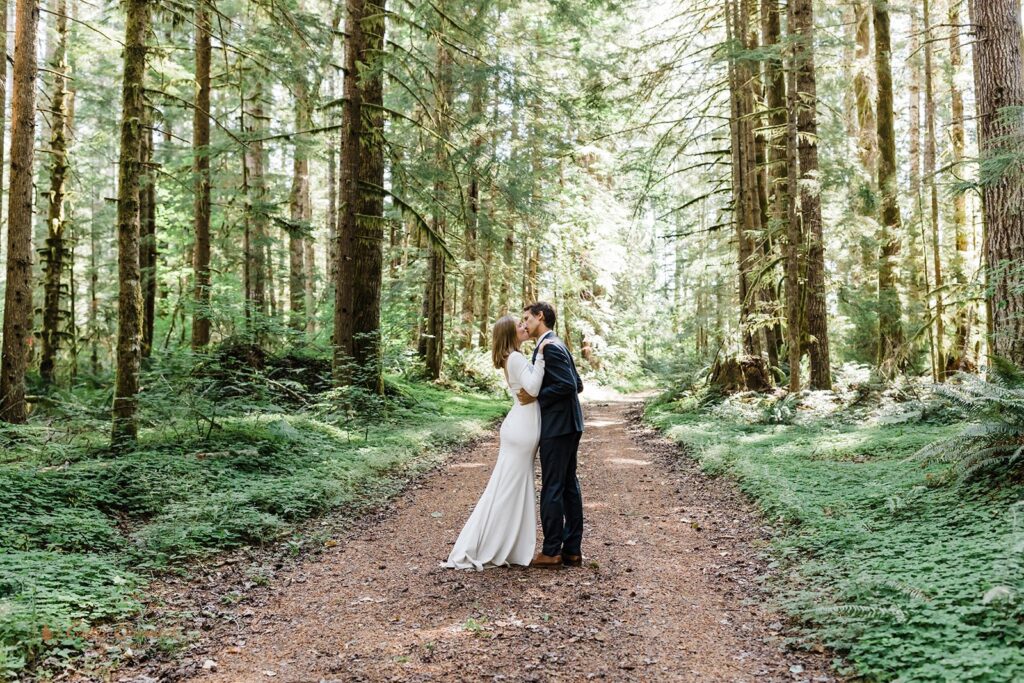 A couple kisses in an evergreen forest   during their Mt. Rainier hiking elopement. 