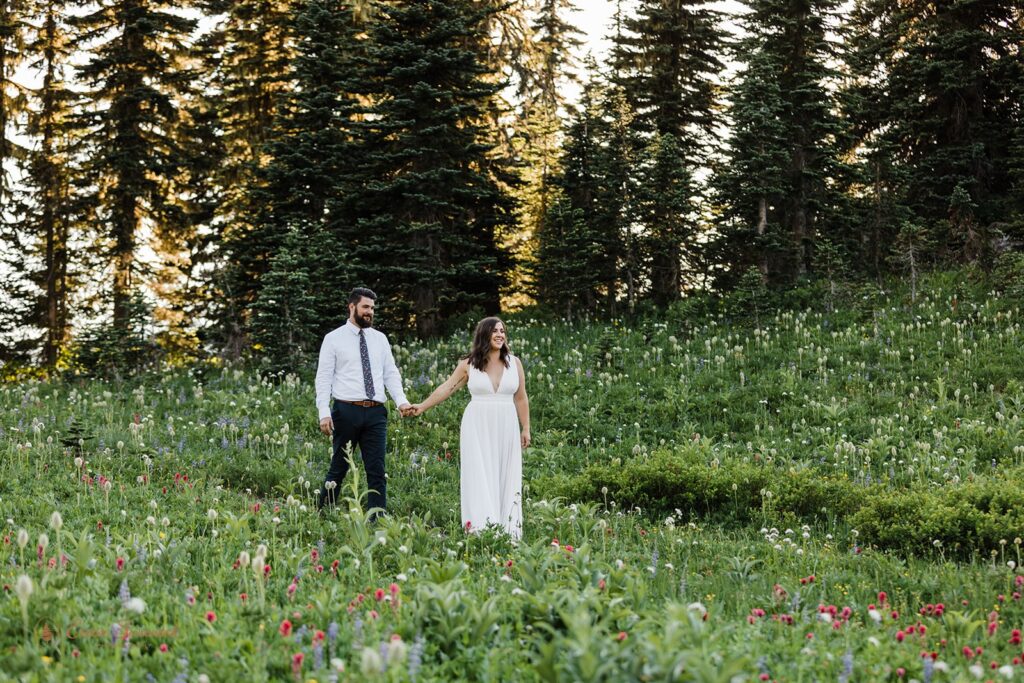 A hiking elopement couple walks along a wildflower meadow trail in Mt. Rainier National Park. 