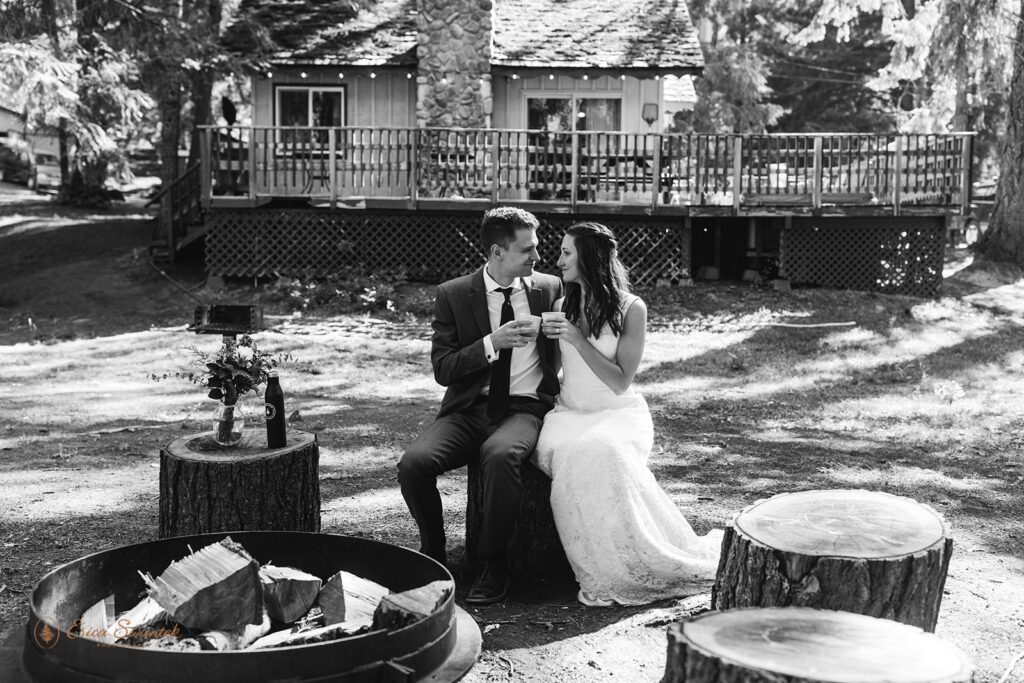 An adventure elopement couple cheers with cups of coffee at Whistlin' Jack's around a fire pit before their outdoor wedding ceremony. 