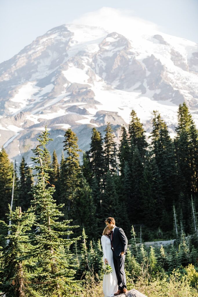 A couple hugs while standing on a rock that looks out onto Mt. Rainier National Park during their elopement. 