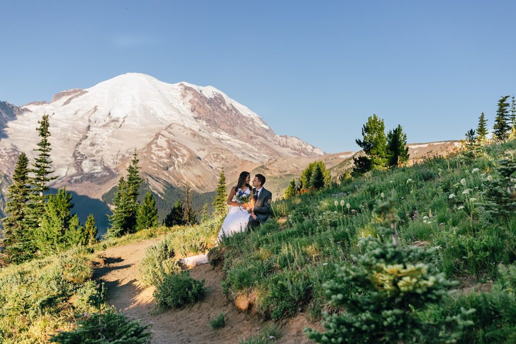 A couple cuddles close on a hillside whiling celebrating a wildflower elopement with Mt. Rainier in the background
