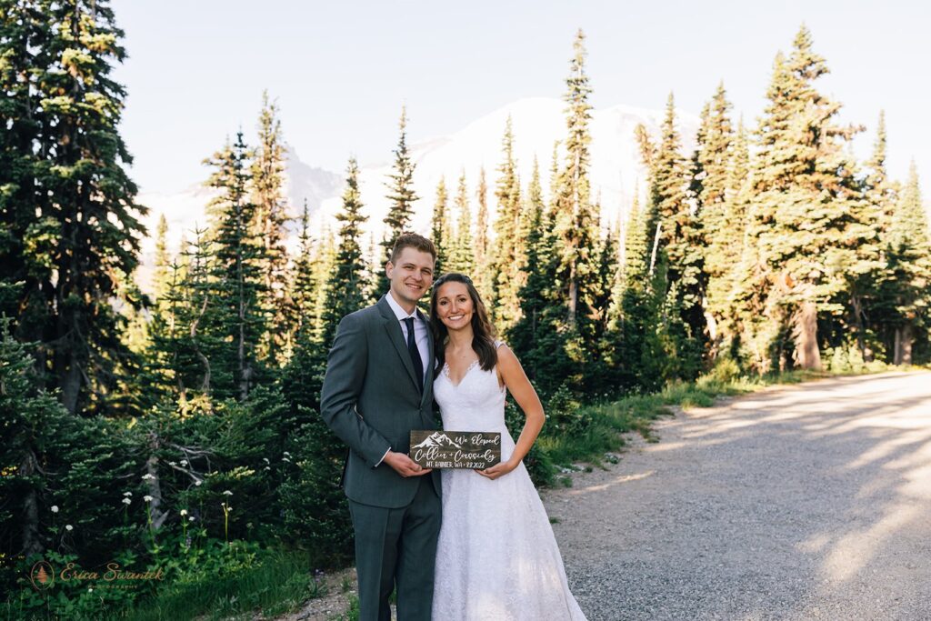 An adventure elopement couple holds a sign that reads "we elopement" in Mt. Rainier National Park. 
