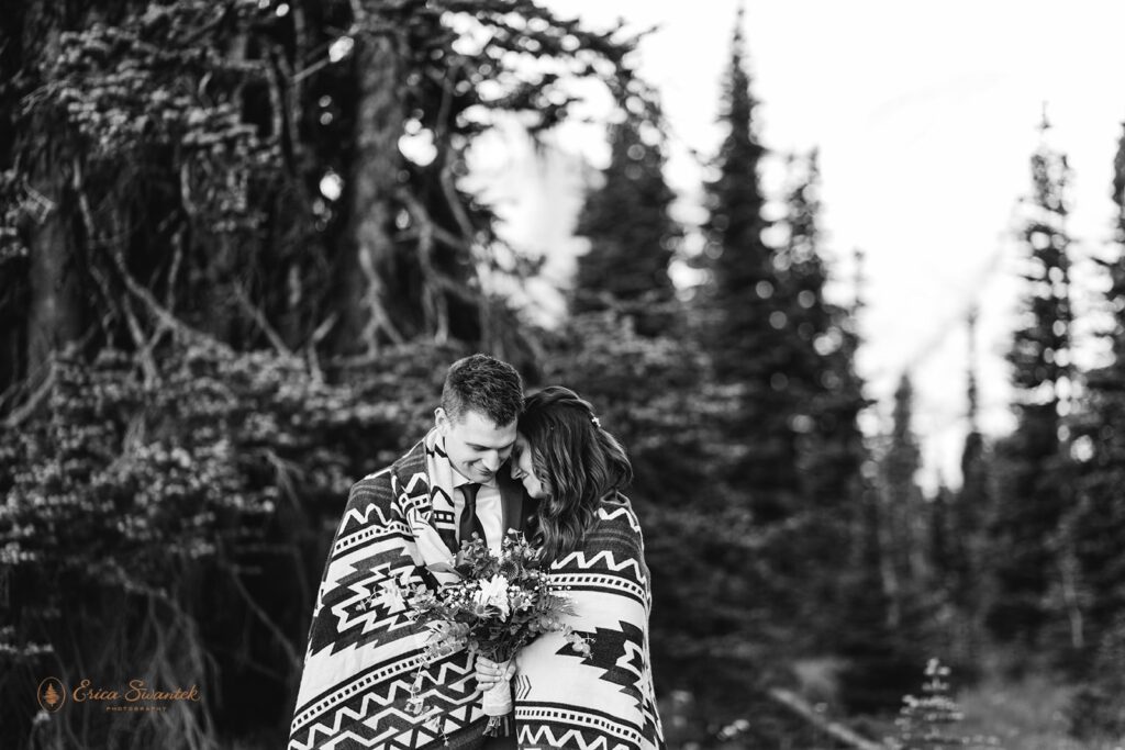 An adventure elopement couple cuddles close with one another under a printed blanket at Mt. Rainier National Park Sunrise Area. 