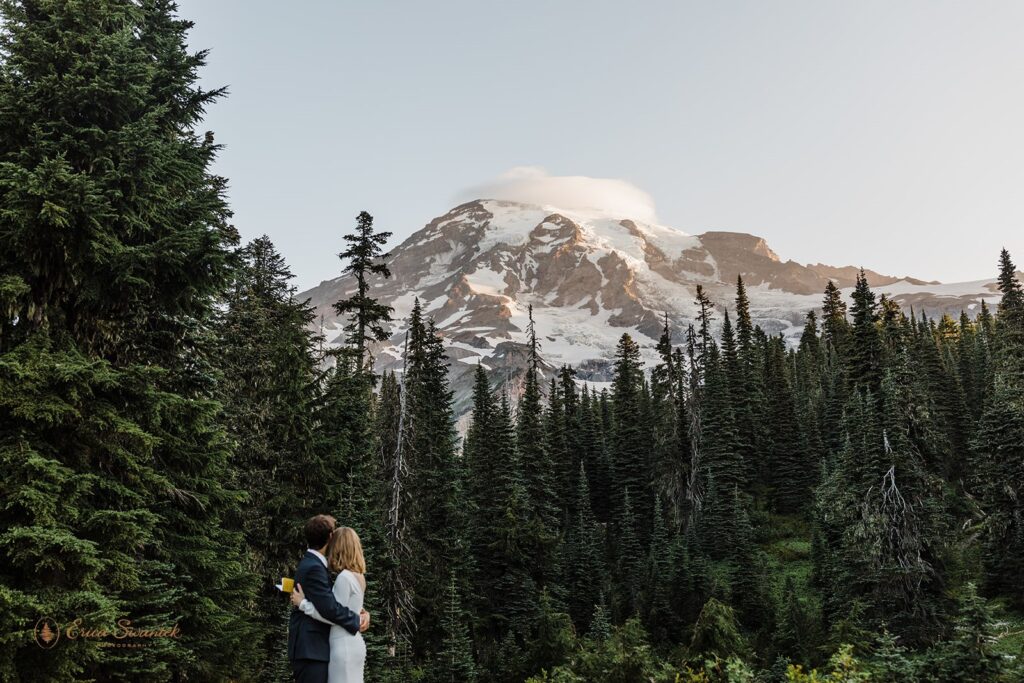 An elopement couple embraces while admiring a snow-capped Mt. Rainier. 