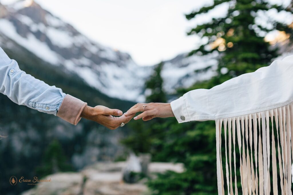 A couple's hands are show wearing engagement rings with the North Cascades in the background.