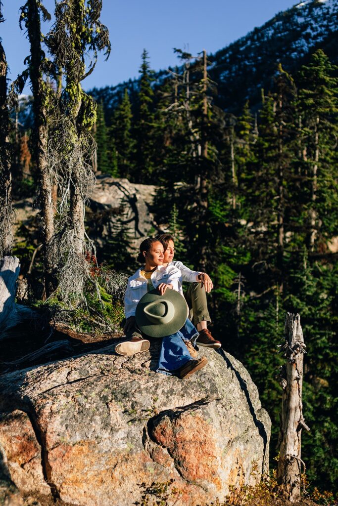 A couple sits on a rock and looks off into the distance during their North Cascades couples session. 