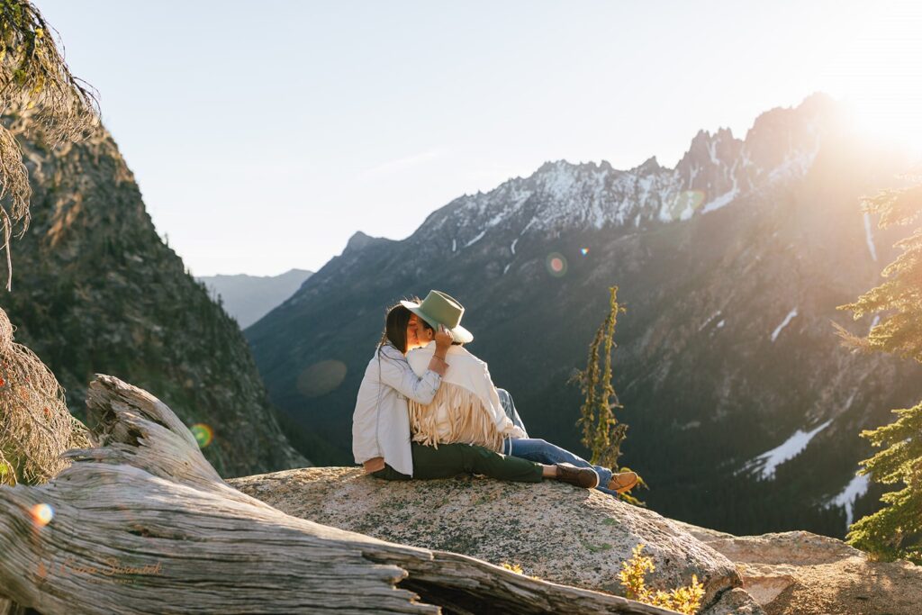 A couple sits on a rock while kissing in the North Cascades. 