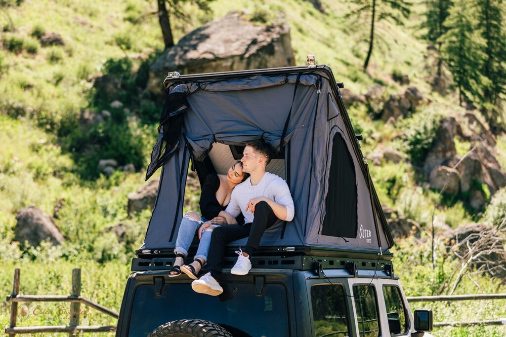 A Washington engagement session couple embraces while holding hands as they sit in a roof top tent on a Jeep. 