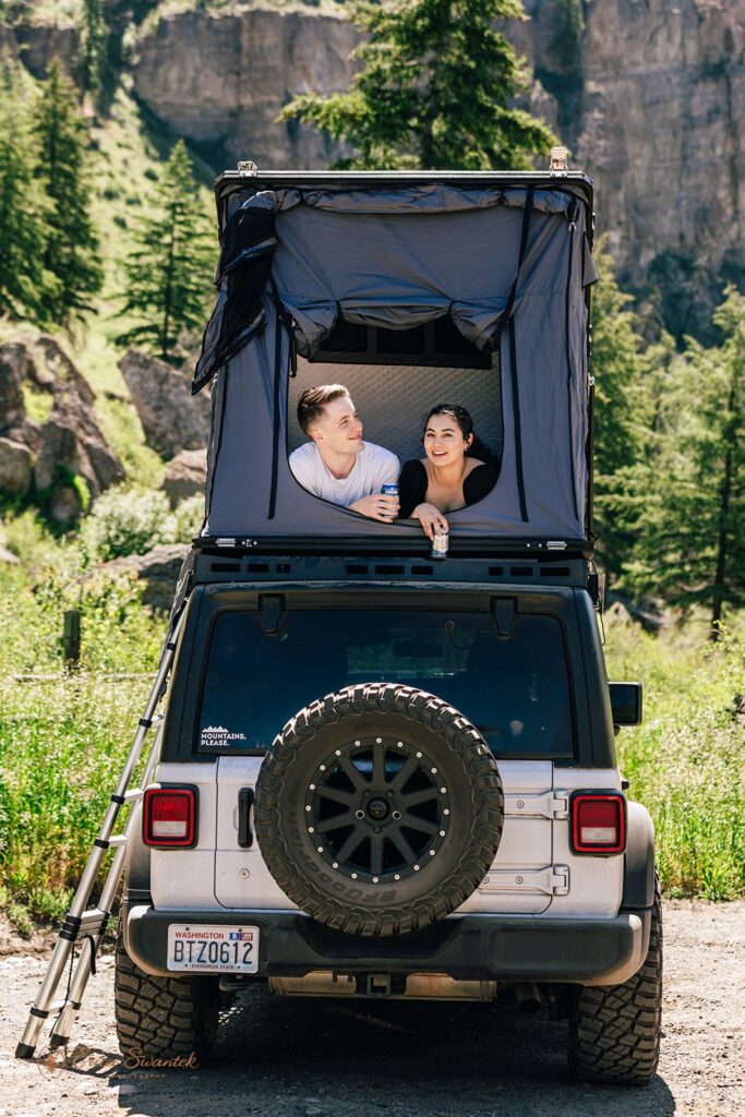 A couple lays in a roof top tent on a Jeep while sharing beers during their North Cascades engagement session. 