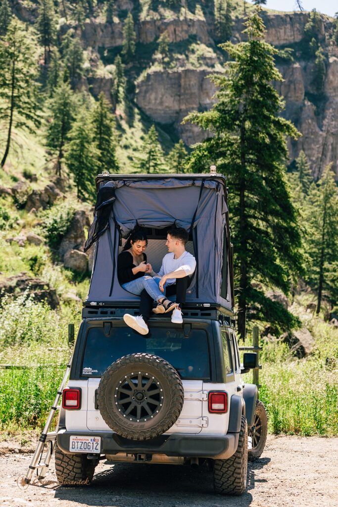 A couple sits in a roof top tent on a Jeep during their Washington engagement session. 