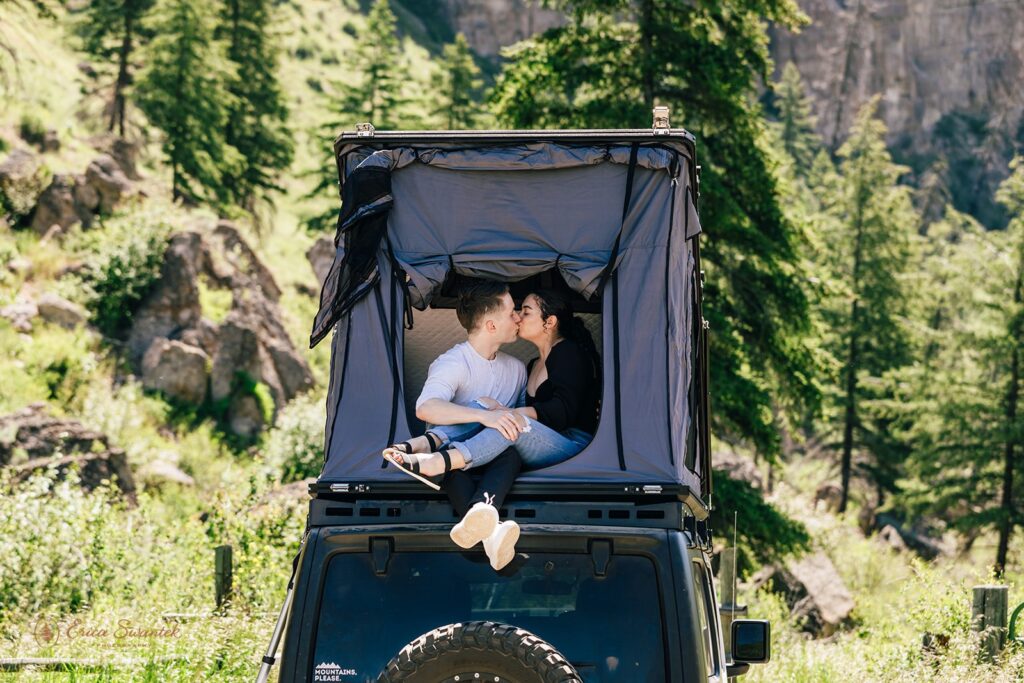 A couple kisses in a roof top tent on a Jeep while sharing beers during their North Cascades engagement session.