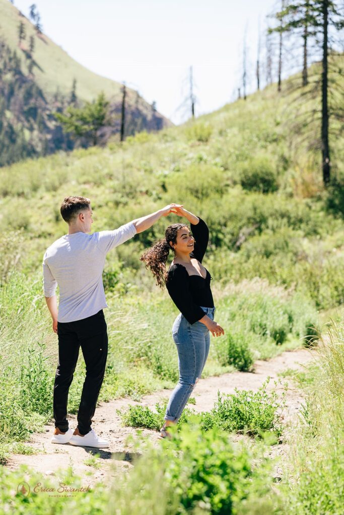 A man twirls his fiancée during their Washington couples session on a hiking trail. 