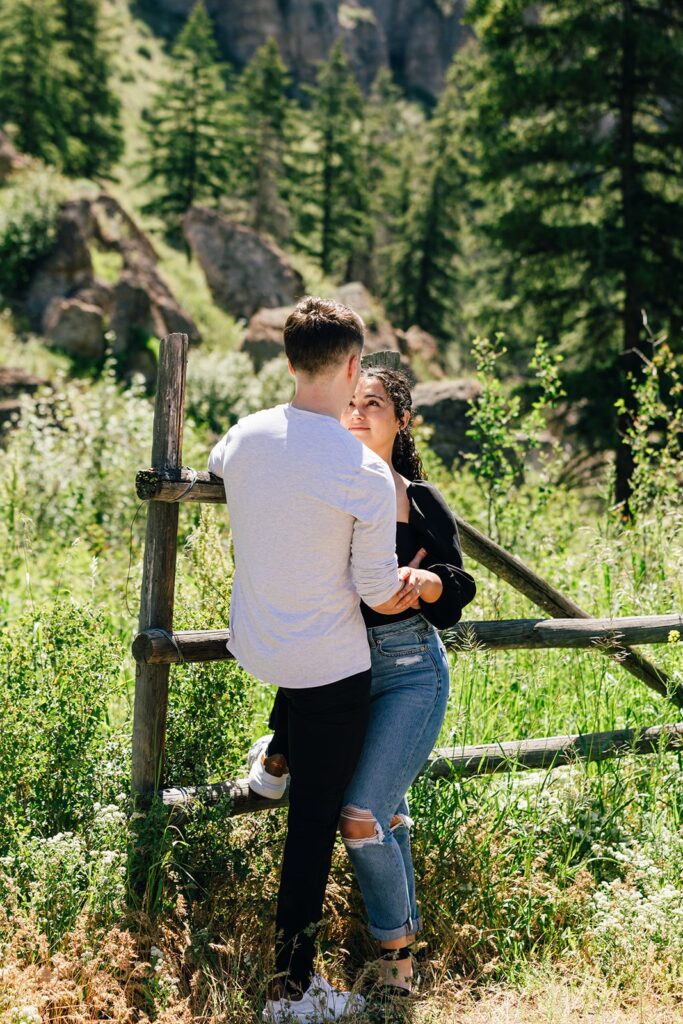 A couple embraces while leaning on a fence during their Washington couples session on a hiking trail in the North Cascades