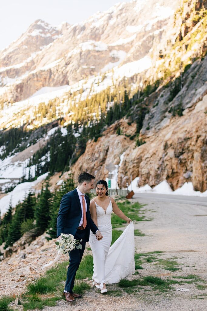 A couple walk along a hiking trail while holding hands during their North Cascades elopement at Washington Pass.
