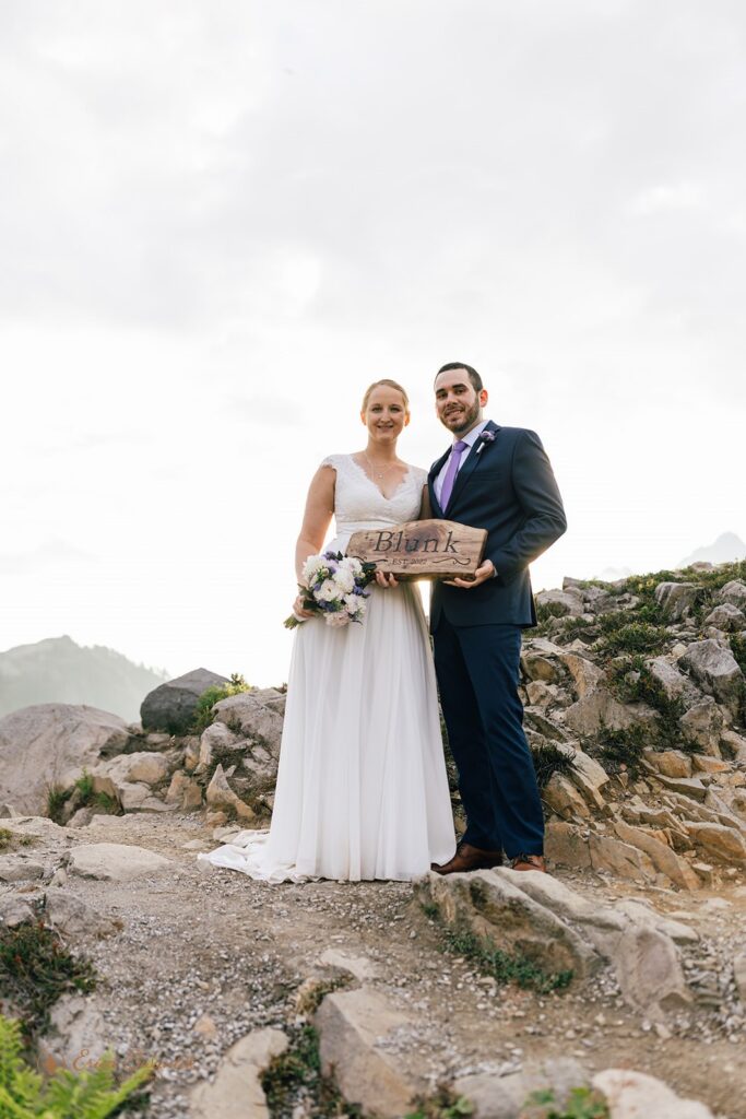 An adventure elopement couple holds a wooden sign on a Washington hiking trail. 