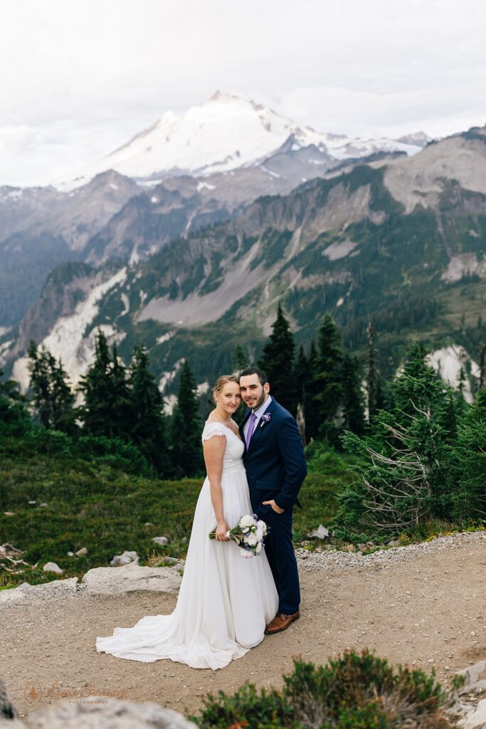 A bride in an a-line wedding gown embraces her groom, who is wearing a navy wedding suit, during their North Cascades elopement. 
