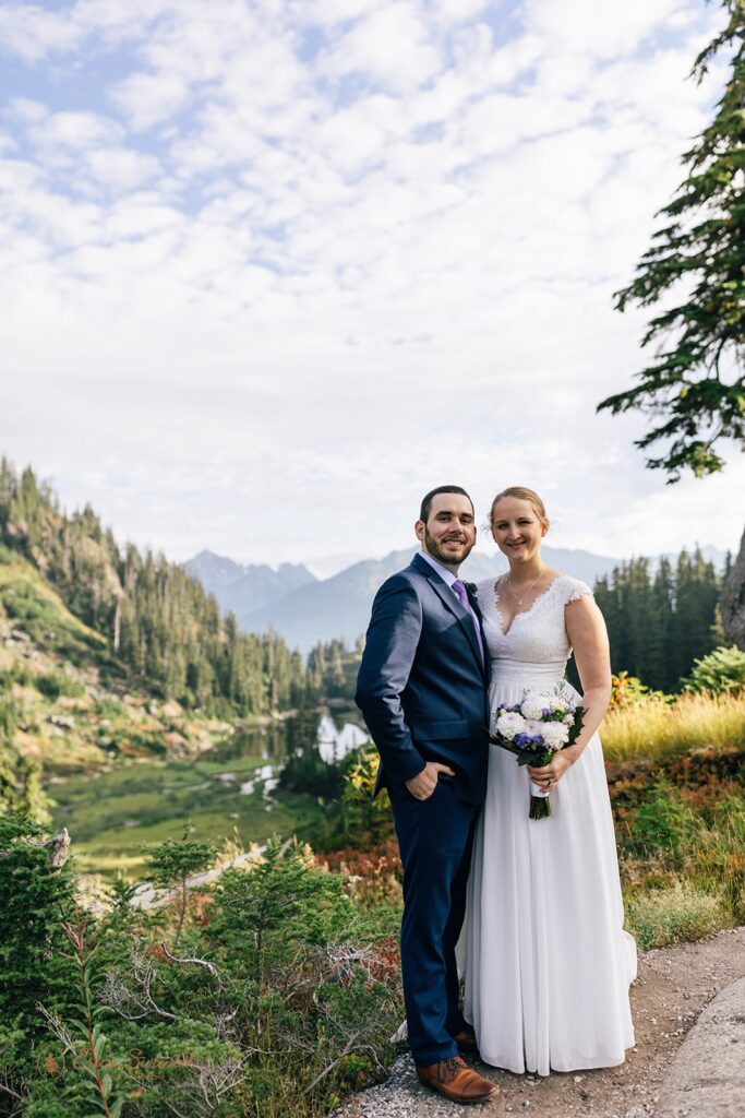 A couple poses for a smiling wedding portrait along a Washington hiking trail at Reflection Lakes during their hiking elopement. 