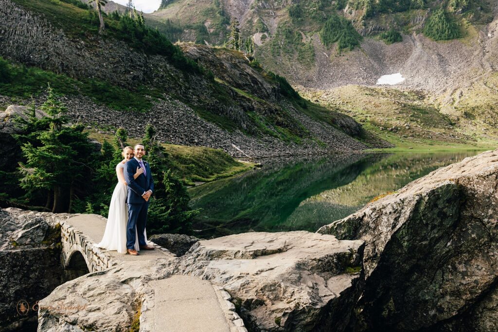 A couple in formal wedding attire stands on a stone bridge at Bagley Lakes during their Washington elopement. 