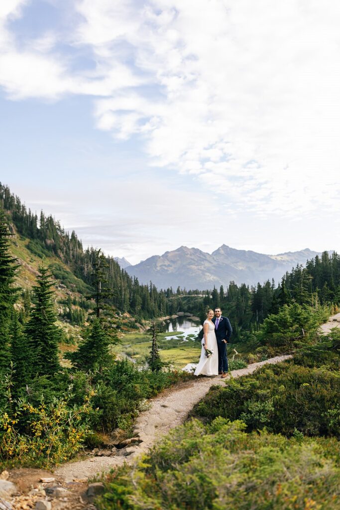 A Washington elopement couple stands along a trail and takes a wedding portrait in front of Reflection Lakes. 