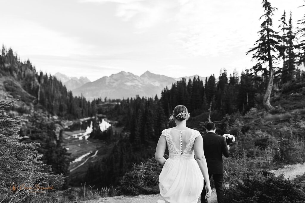 A groom holds his bride's bridal bouquet as they walk along a North Cascades hiking trail in Washington. 