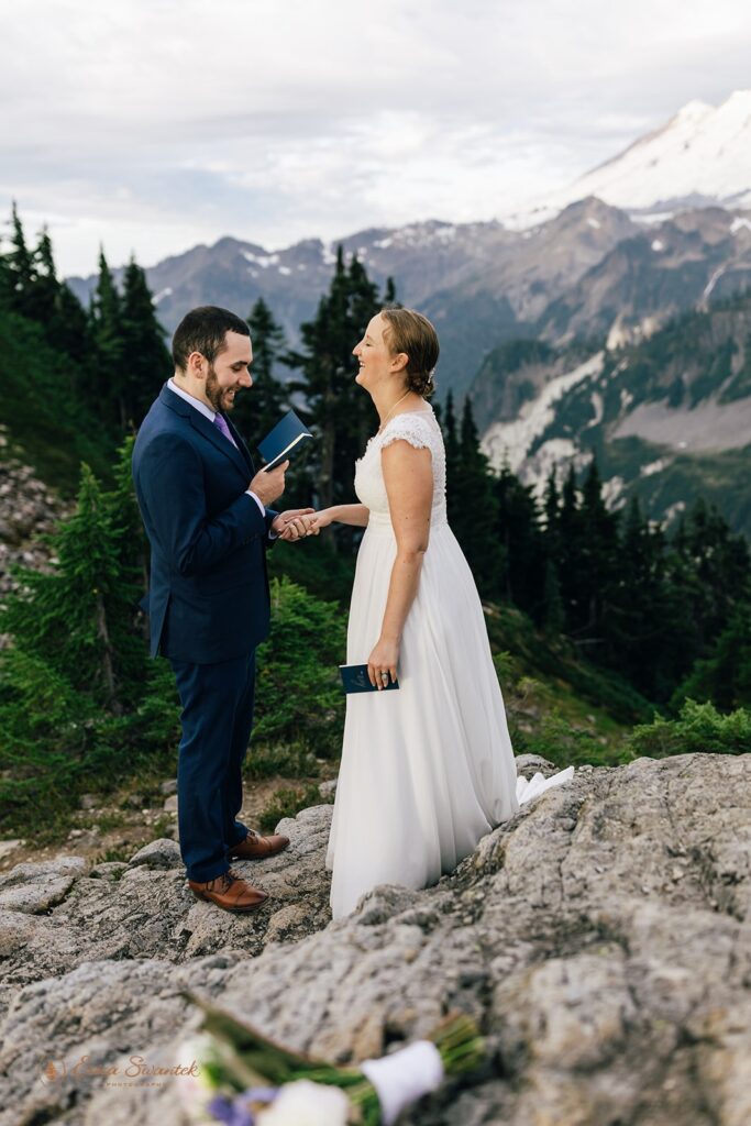 A groom in a navy suit holds his bride's hand as he recites intimate vows during their North Cascades elopement. 