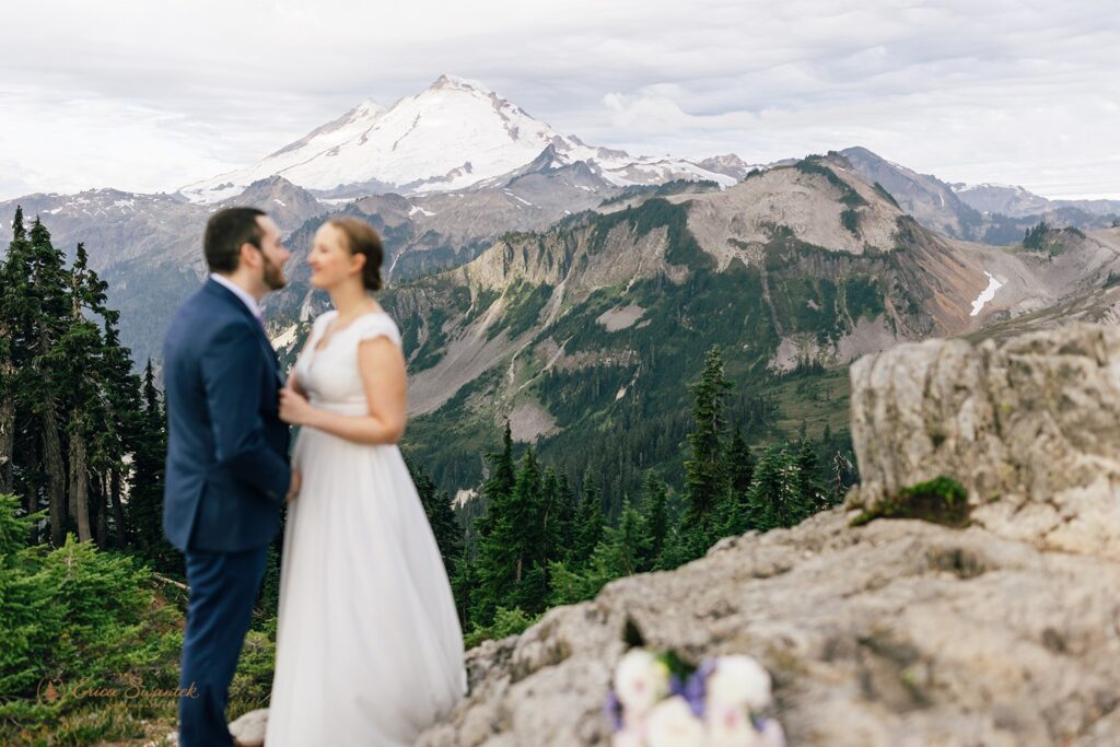 A North Cascades elopement couple stands close to one another with snowy Mt. Baker in the distance. 